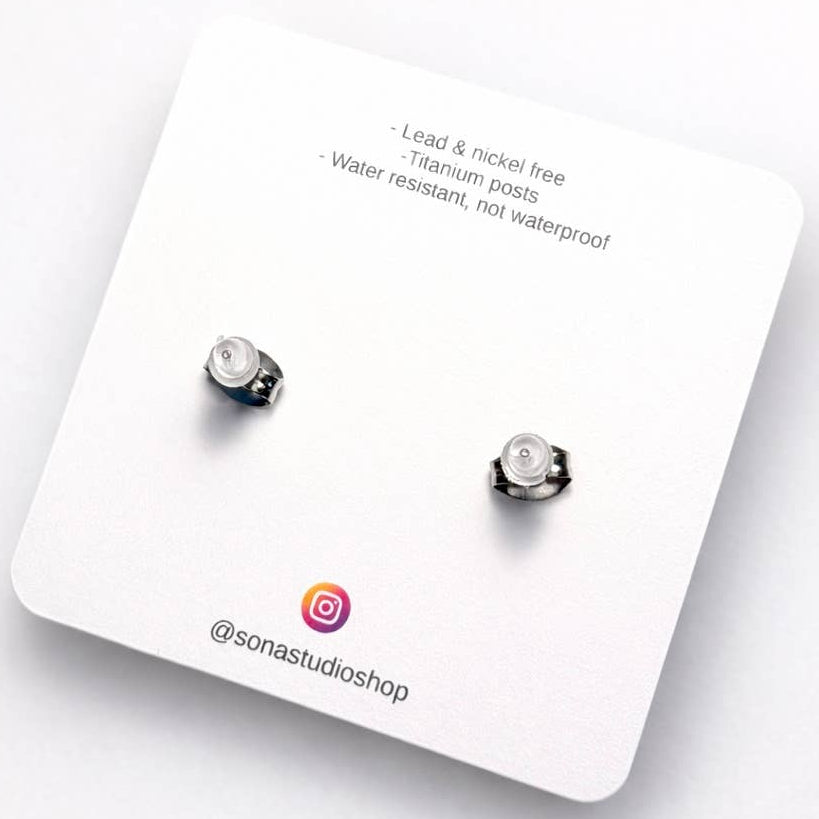 Pair of silver stud earrings on a white card with product details.