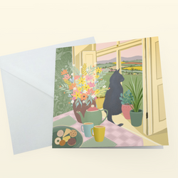 A greeting card with a whimsical illustration of a black cat sitting by a window with flowers, plants, and a tea set