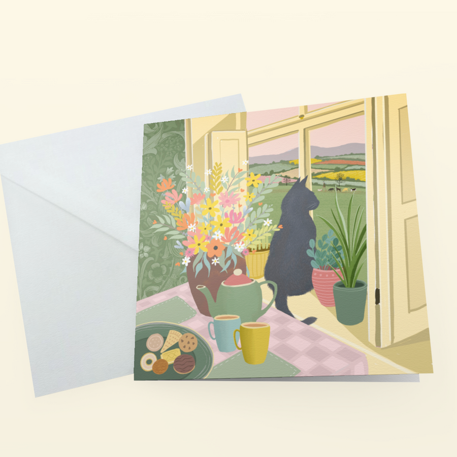 A greeting card with a whimsical illustration of a black cat sitting by a window with flowers, plants, and a tea set
