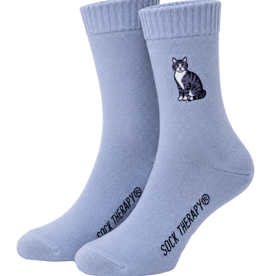 A pair of light blue crew socks with a small black and white cat graphic on the front sock. 