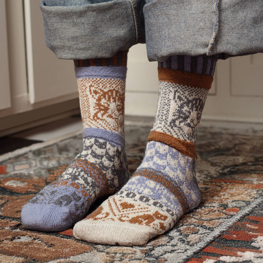Person wearing cat patterned socks with rolled-up jeans on a rug.