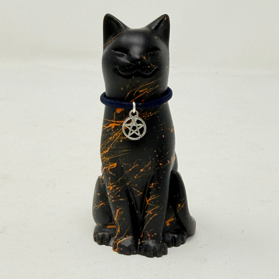 A black cat resin figurine with orange splatter details, wearing a dark blue cord collar with a silver pentagram pendant