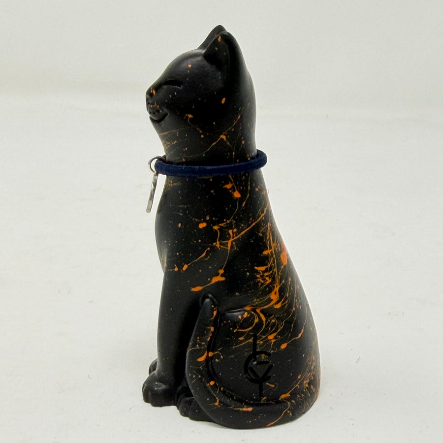 A black lucky cat resin figurine with orange marbled splatters and a dark blue collar