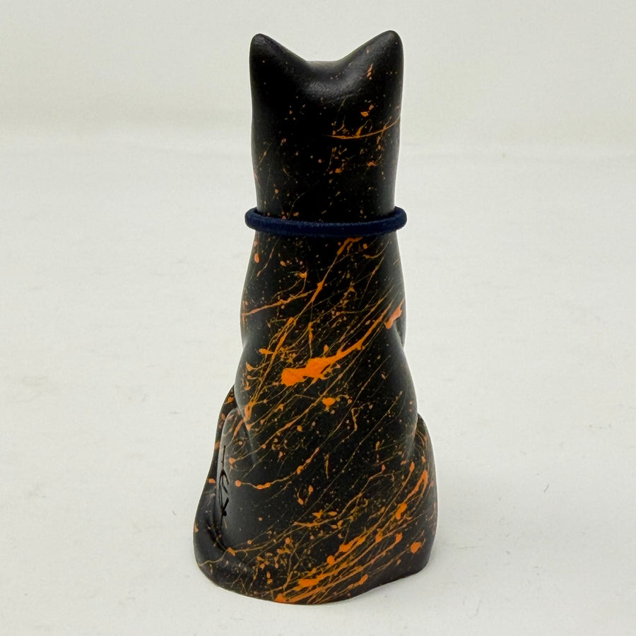 A black lucky cat resin figurine with orange splatter details and a dark blue collar, shown from the back against a plain white background.