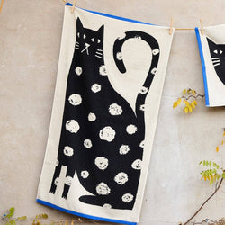 Two towels with cat designs hanging on a line against a neutral background