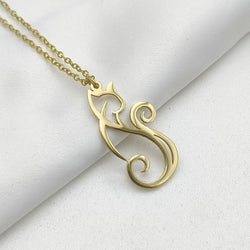 A gold necklace with a stylised cat-shaped pendant, displayed on a soft white fabric background.