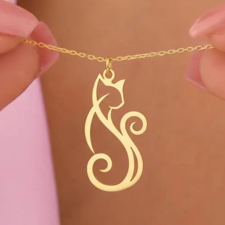 A gold necklace with a stylised cat-shaped pendant, held in a person's fingers by the chain