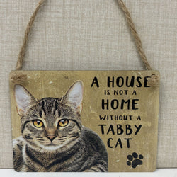 A rustic hanging sign with a photo of a tabby cat and the text 'A HOUSE IS NOT A HOME WITHOUT A TABBY CAT' plus a black paw print, suspended by twine