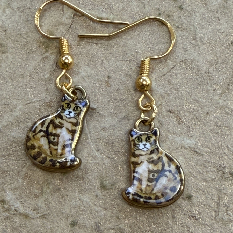 A pair of gold-tone dangle earrings featuring ceramic cat charms with brown, black, and cream tabby patterns