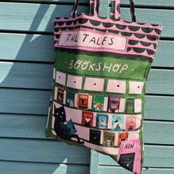 A pink and green fabric tote bag with 'TAIL TALES BOOKSHOP' printed on it, featuring a black cat reading a book and book covers on the front