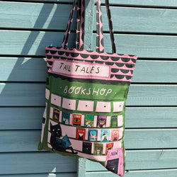 A fabric tote bag with a bookshop theme, featuring a green and pink design with a black cat and book illustrations