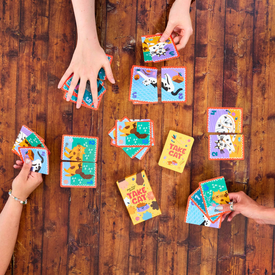 Colourful card game Take Cat being played on a wooden table with multiple hands.