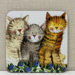 A square decorative coaster featuring an illustration of three cats sitting together on a bed of blue flowers. 