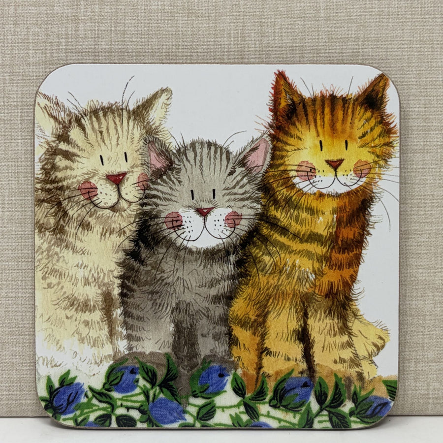 A square decorative coaster featuring an illustration of three cats sitting together on a bed of blue flowers. 