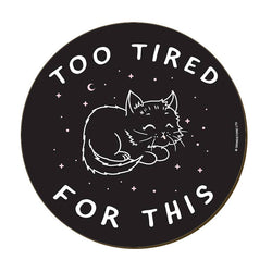 A circular black coaster featuring a white line art illustration of a sleeping cat under a crescent moon and stars, with the text 'TOO TIRED FOR THIS' in white.