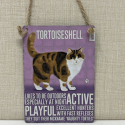 A rectangular hanging sign with a purple background featuring an illustration of a tortoiseshell cat and text that reads 'TORTOISESHELL' and additional cat-related phrases.