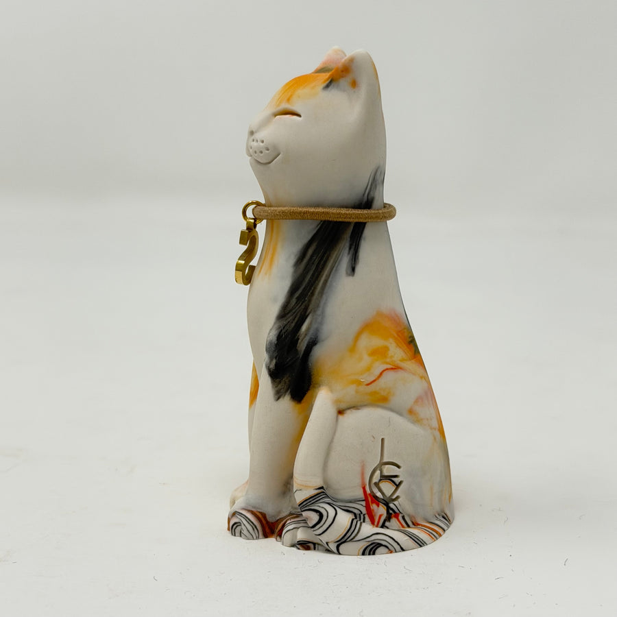 A hand-painted resin Lucky Cat figurine in a sitting position, featuring a white base with orange, black, and yellow marbled patterns, gold collar, and a patterned tail