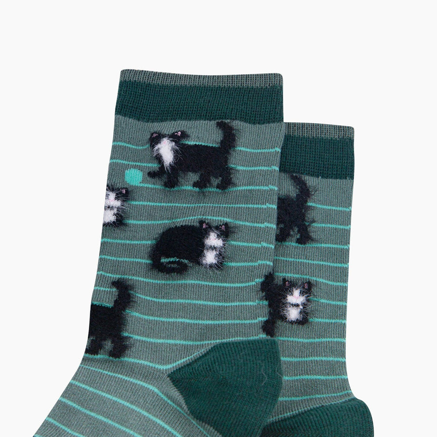 A pair of crew socks in a muted green color with thin mint green horizontal stripes and a pattern of black and white cats