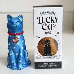 A blue Lucky Cat figure decorated with white stars, red collar and American flag medallion, shown next to its white and black retail packaging box labelled 'The Original Lucky Cat York'.