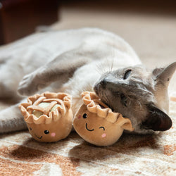 Cat playing with two plush pie toys with anthropomorphic faces on a textured surface