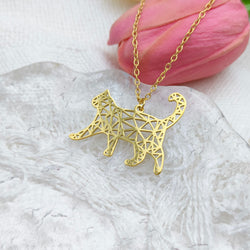 Gold geometric cat pendant necklace on a white surface with a pink flower in the background
