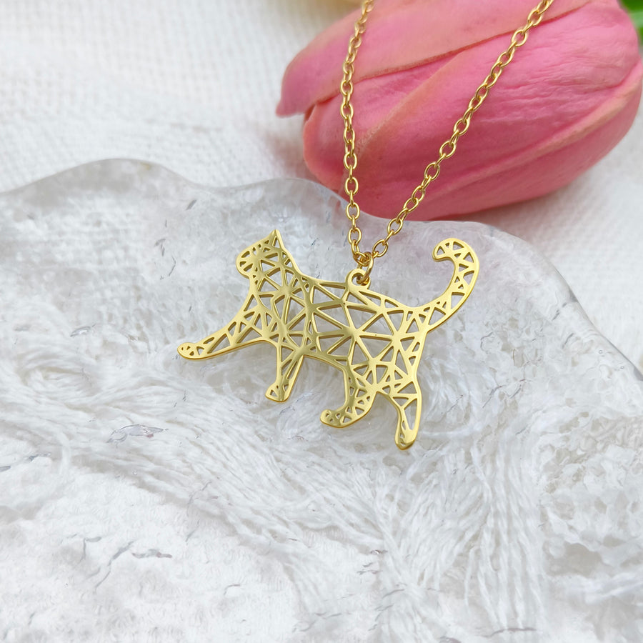 Gold geometric cat pendant necklace on a white surface with a pink flower in the background