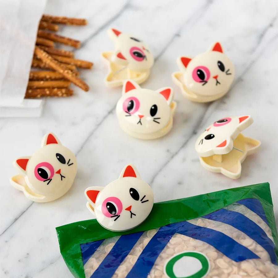 Cat-head shaped bag clips with pink cheeks and orange ears on a marble surface with pretzels.