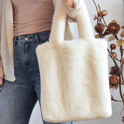 A person holds a large cream faux-fur tote bag with double shoulder straps. 