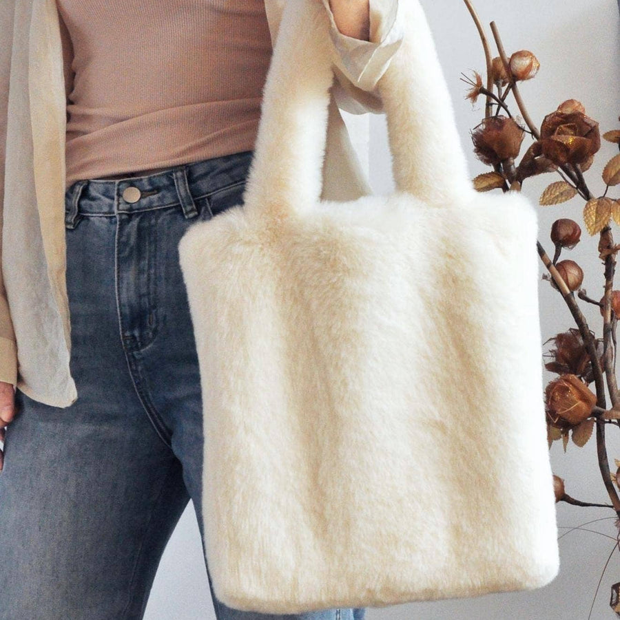 A person holds a large cream faux-fur tote bag with double shoulder straps. 