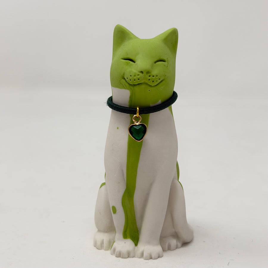 A resin lucky cat figurine with a green and white body, wearing a black collar with a green heart-shaped charm
