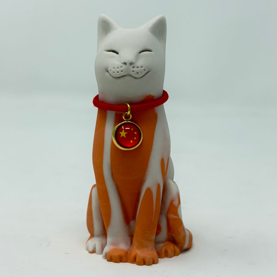 A resin lucky cat figurine in white and orange, wearing a red collar featuring the Chinese flag.