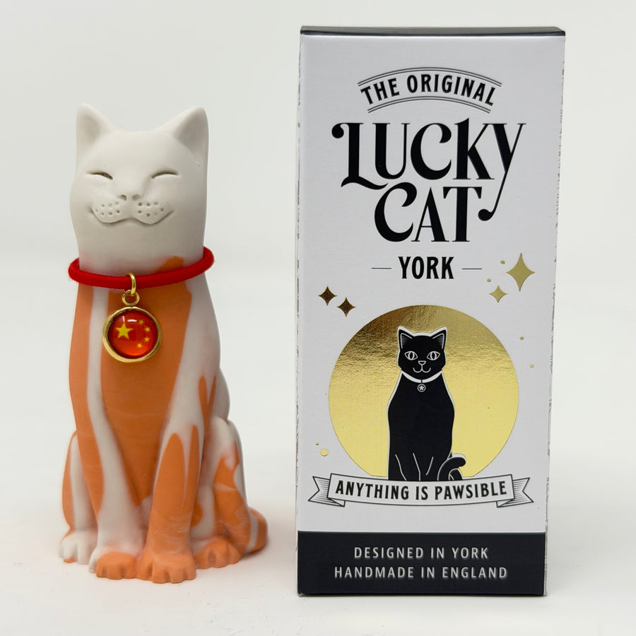 A white and orange resin lucky cat figurine wearing a red collar with a red flag, shown next to its retail box labeled 'The Original Lucky Cat York'.