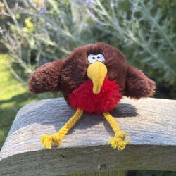 A small plush robin  toy with brown wings, a yellow beak and legs, and a red fluffy chest