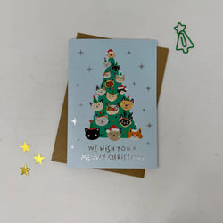 A Christmas greeting card featuring a light blue background with a green Christmas tree made of cute illustrated cats wearing Santa hats. 