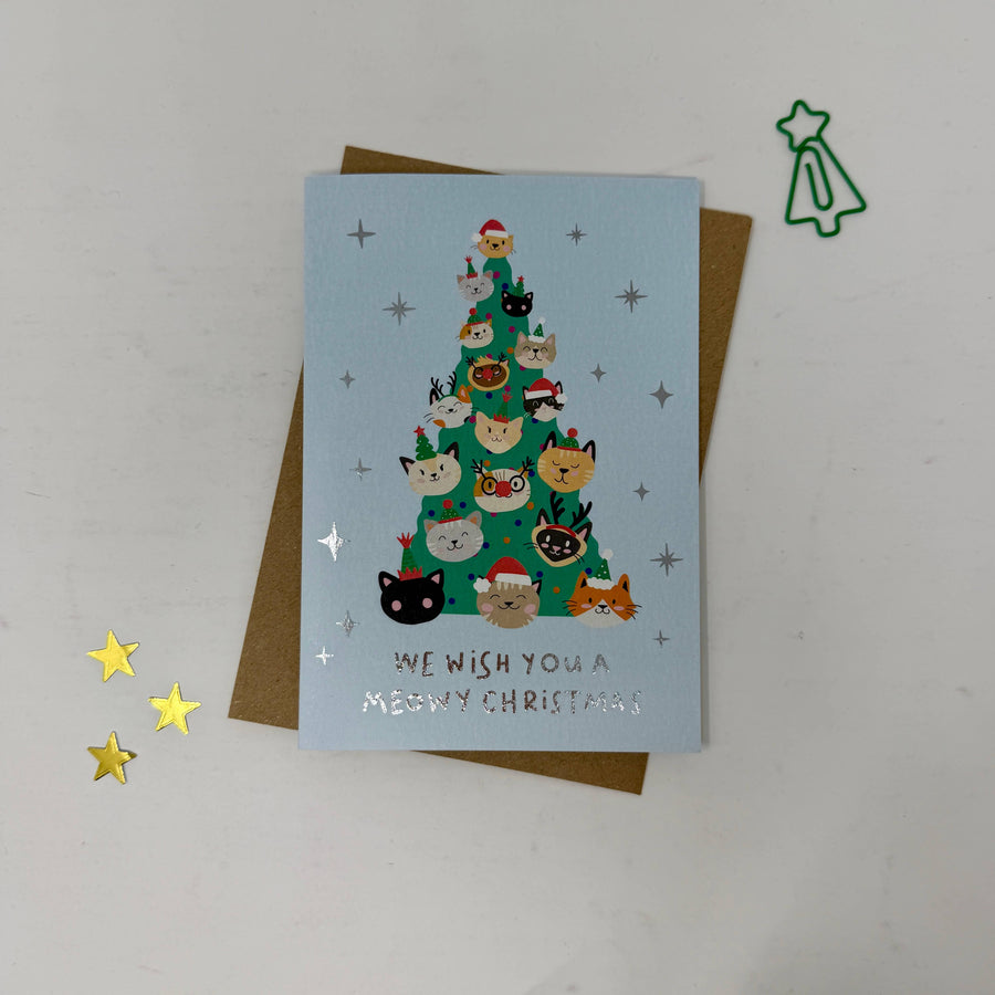 A Christmas greeting card featuring a light blue background with a green Christmas tree made of cute illustrated cats wearing Santa hats. 