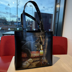 Black tote bag with a cat and candle design on a table indoors