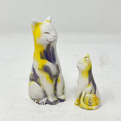 Two marbled smiling lucky cat figures in shades of yellow, purple and white on a light grey background