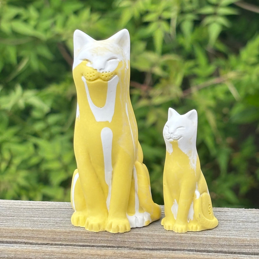 Yellow and White lucky cat figurines on a wooden surface with a green foliage background