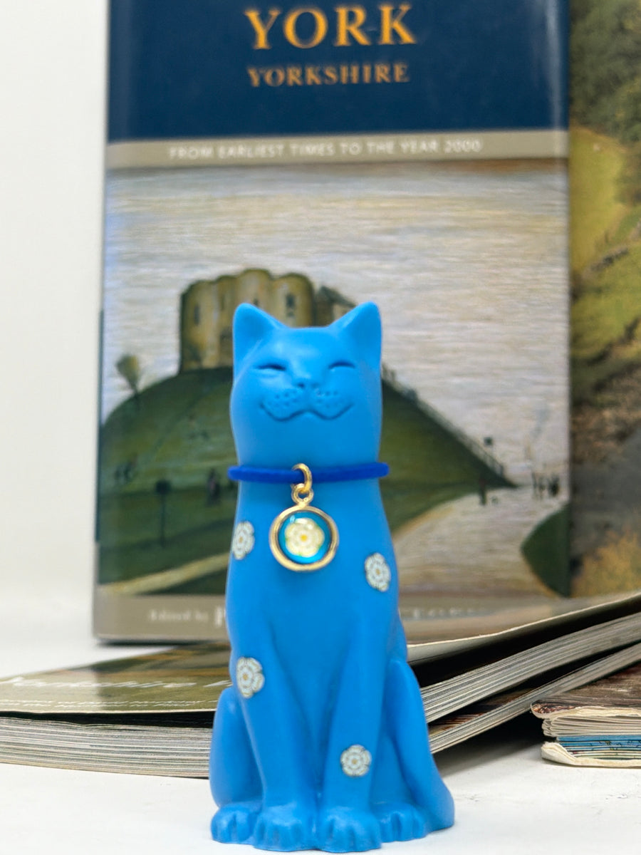 Yorkshire Rose blue cat with blue collar and yorkshire rose charm displayed in front of a book with Cliffords Tower York on the cover