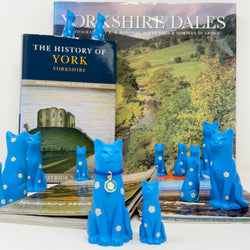 Cat and kitten blue ornaments decorated with white roses with blue collar with round white rose charm, displayed with books about Yorkshire