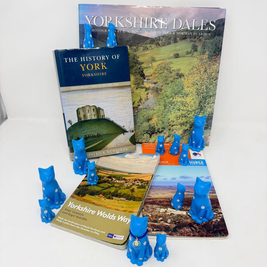 Many blue cats and kitten ornaments decorated with white roses, the larger cats with blue collar with round white rose charm, displayed with books about Yorkshire