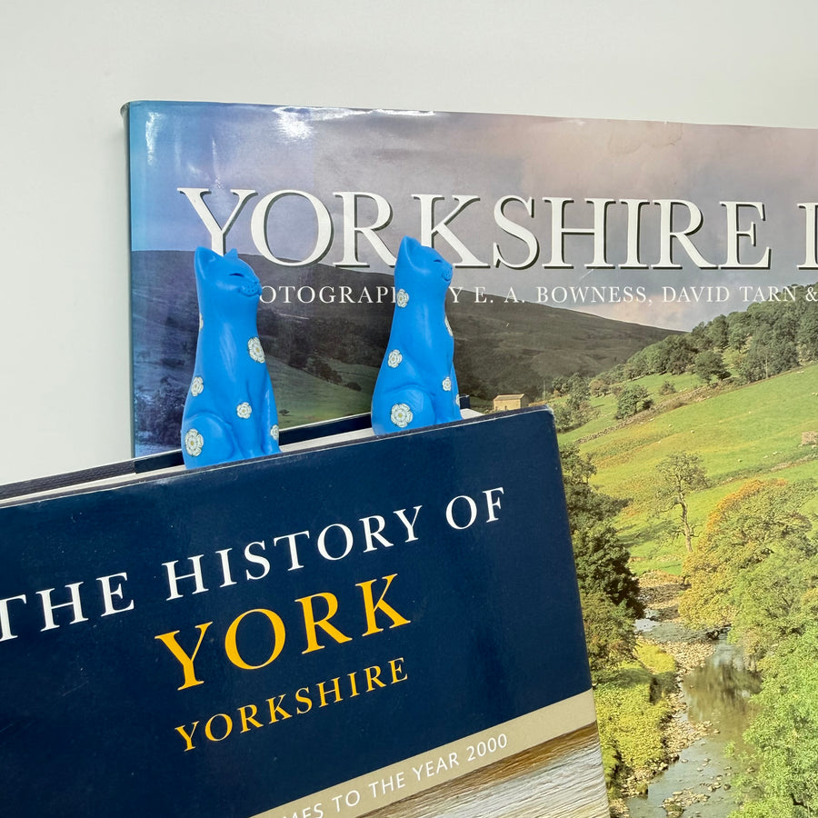 Two blue kitten ornaments decorated with white roses, displayed with books about Yorkshire
