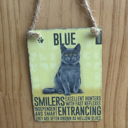 A rectangular metal hanging sign, with grey cat illustration and the word 'BLUE' at the top. The sign includes text describing alleged attributes of blue cats and is suspended by twine against a wooden wall.