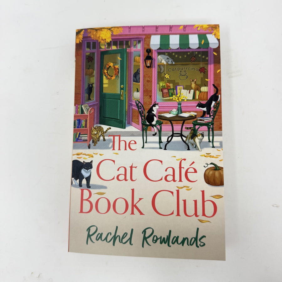 The Cat Café Book Club book by Rachel Rowlands, featuring a colourful illustration of a cat cafe storefront with cats and autumn leaves, photographed on a white background.