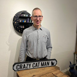 Cat Gallery owner standing in front of a sign saying "Crazy Cat Man" and with a silhouette of a black cat
