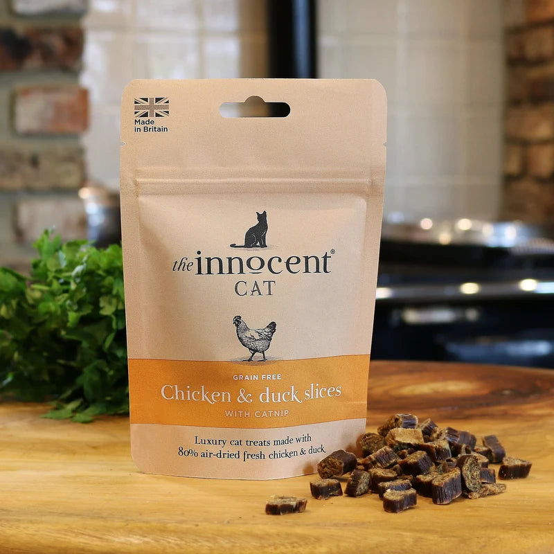 Innocent Cat Chicken & Duck Slices with Catnip pack front - lifestyle shot with scattered treats visible