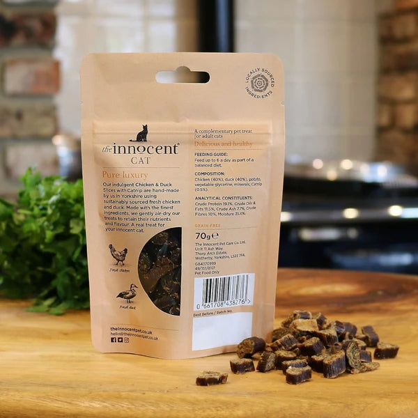 Rear view of 70g pouch of innocent cat chicken and duck slices on a wooden kitchen surface with treats visible outside the packet