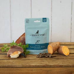 Pack shot of innocent cat tuna and crab treats  on a wooden surface with scattered treats
