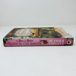 A hardback copy of the book 'Agnes Aubert's Mystical Cat Shelter' by Heather Fawcett, showing the pink spine and illustrated front cover on a white background.