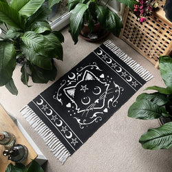 Black rug with white tassels with mystical white cat motif featuring pentagram stars and moons in a lifestyle setting